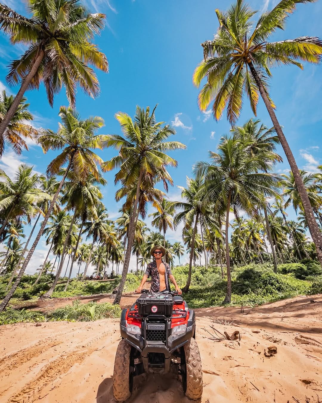 Viajante em um quadriciclo vermelho entre coqueirais na Península de Maraú